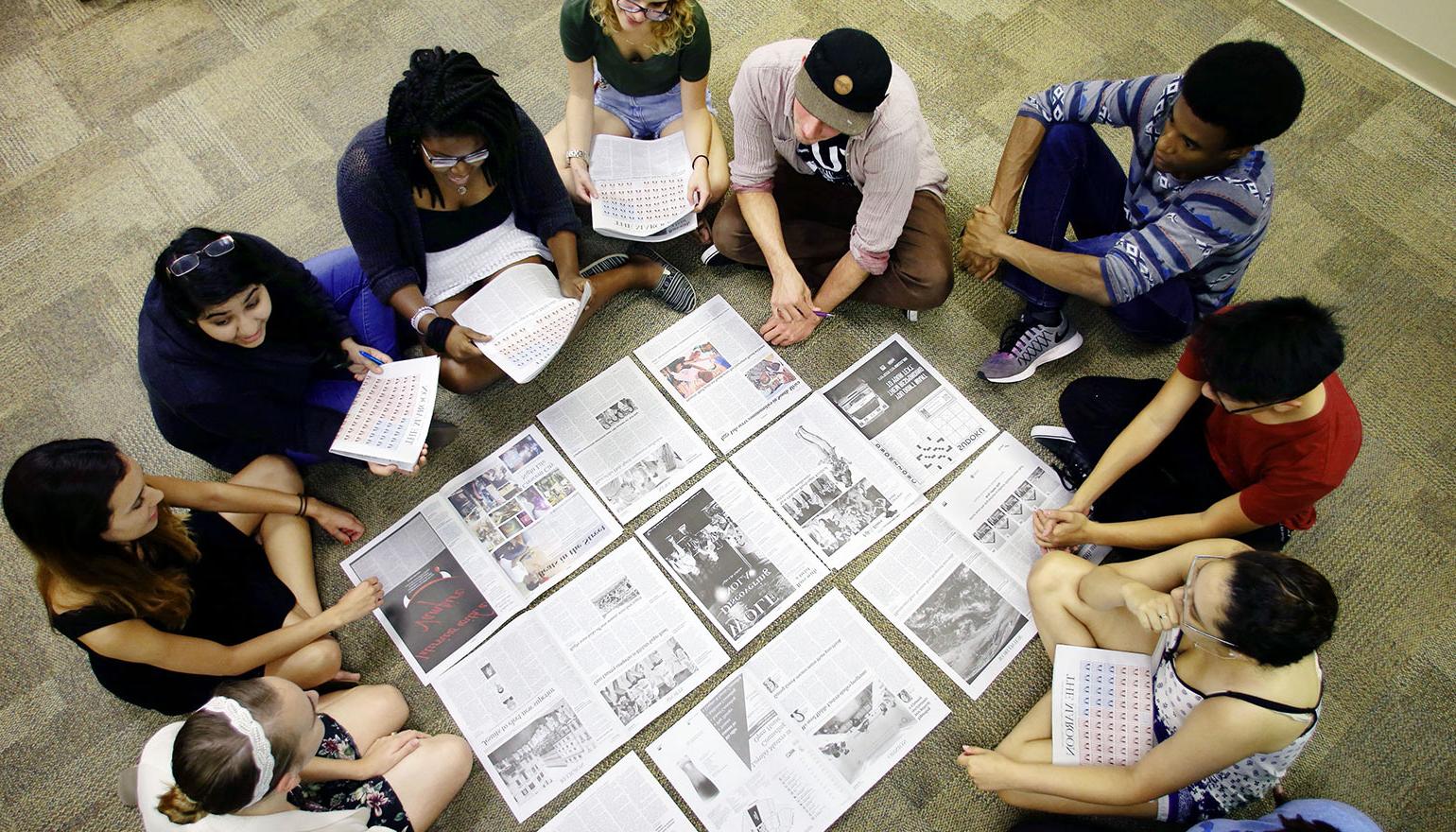 Students surrounding print outs of newspaper draft